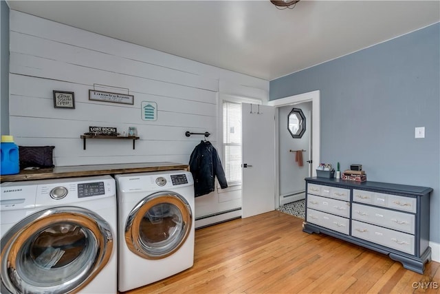 laundry area featuring wooden walls, washer and dryer, a baseboard radiator, and light hardwood / wood-style floors