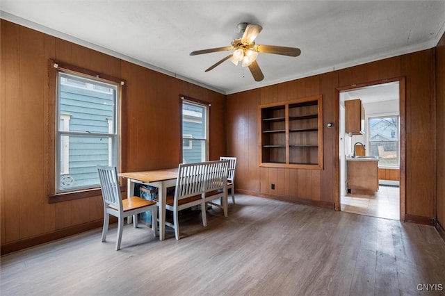 dining room with hardwood / wood-style floors, wooden walls, ceiling fan, built in features, and ornamental molding