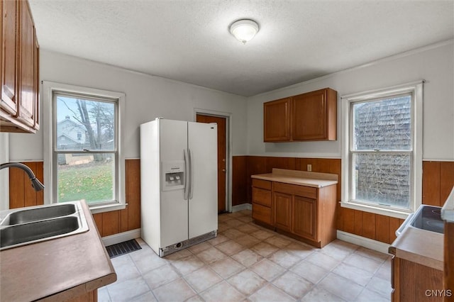 kitchen featuring a textured ceiling, wooden walls, sink, and white refrigerator with ice dispenser