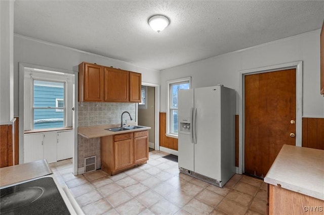 kitchen featuring backsplash, a textured ceiling, wooden walls, sink, and white refrigerator with ice dispenser