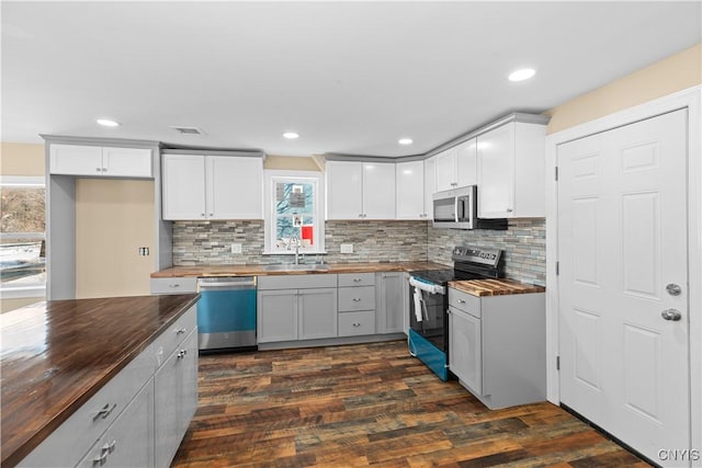 kitchen with appliances with stainless steel finishes, dark hardwood / wood-style flooring, butcher block countertops, and white cabinetry