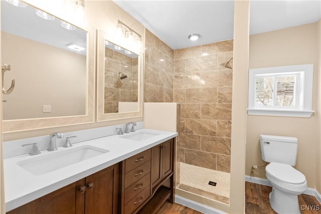 bathroom featuring a tile shower, hardwood / wood-style floors, vanity, and toilet