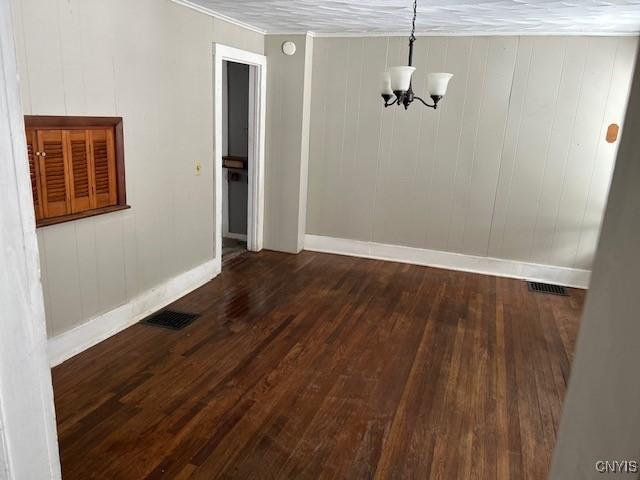 unfurnished dining area with dark hardwood / wood-style flooring, crown molding, and an inviting chandelier