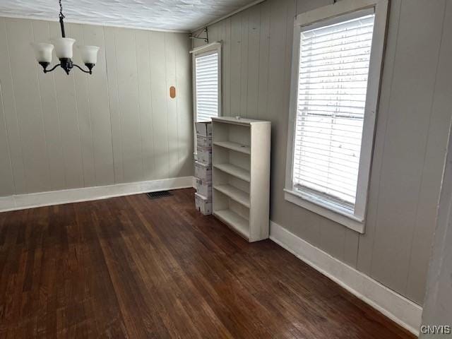 empty room featuring dark wood-type flooring, a notable chandelier, and a wealth of natural light