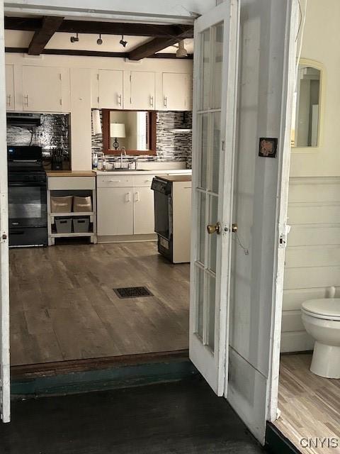 kitchen featuring beamed ceiling, white cabinets, dark wood-type flooring, and stove