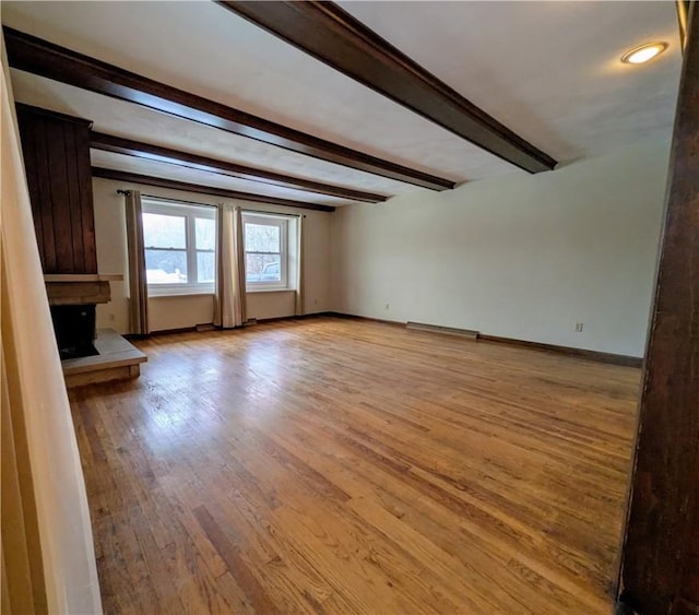 unfurnished living room with beamed ceiling and light wood-type flooring