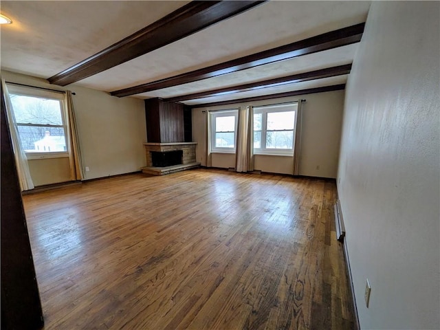 unfurnished living room featuring beam ceiling, a wealth of natural light, a fireplace, and hardwood / wood-style flooring