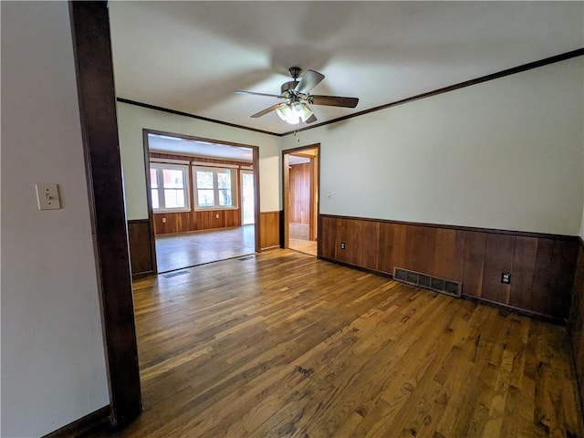 spare room featuring dark hardwood / wood-style flooring, ceiling fan, crown molding, and wood walls