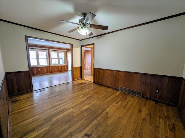 spare room with ceiling fan, dark hardwood / wood-style flooring, wooden walls, and ornamental molding