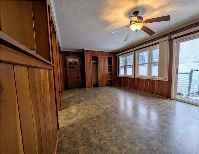 unfurnished living room with ceiling fan, wood walls, and a textured ceiling