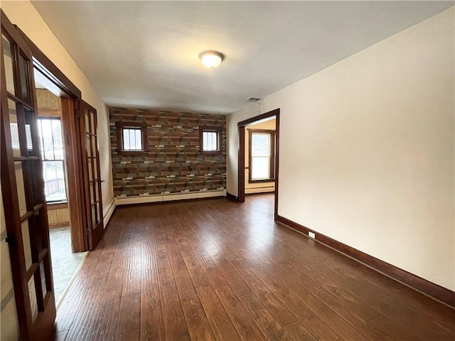 empty room with baseboard heating, plenty of natural light, dark wood-type flooring, and brick wall