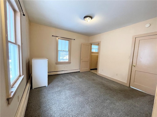 spare room with baseboard heating, a wealth of natural light, and dark carpet