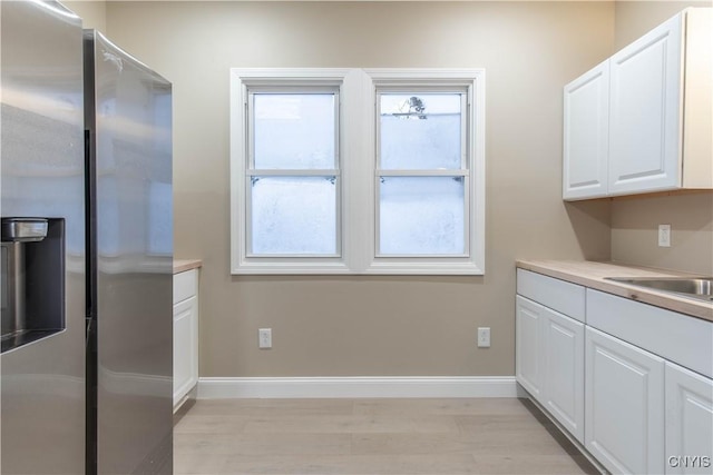 kitchen featuring stainless steel fridge, light wood-type flooring, white cabinetry, and sink