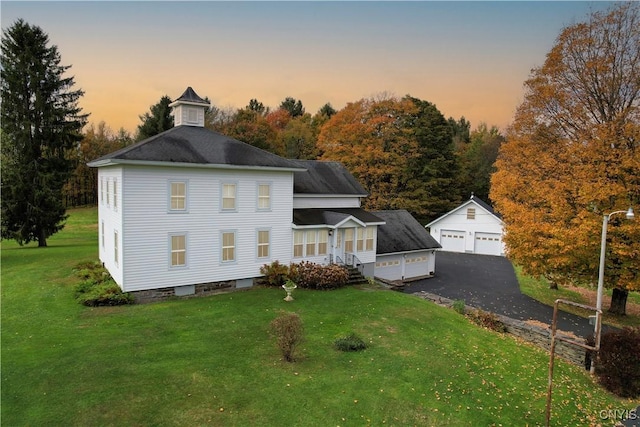 back house at dusk with a garage, a yard, and an outbuilding