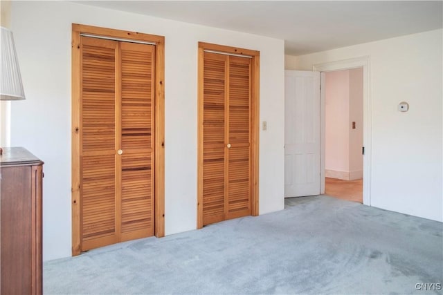 unfurnished bedroom featuring multiple closets and light colored carpet