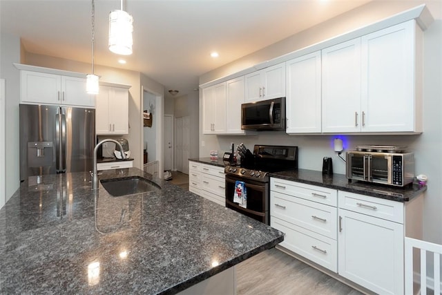 kitchen featuring dark stone counters, stainless steel appliances, sink, decorative light fixtures, and white cabinets