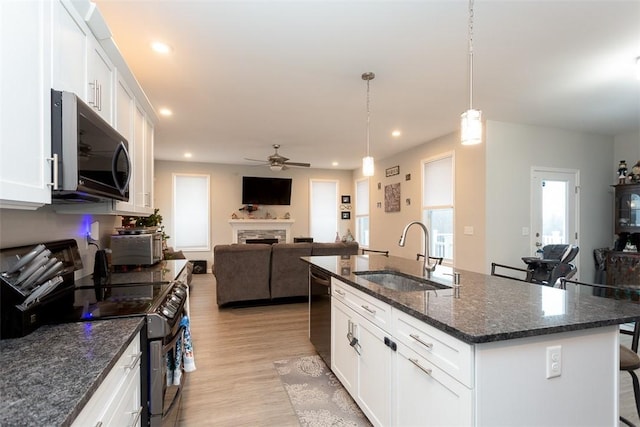 kitchen with white cabinetry, hanging light fixtures, stainless steel appliances, and a center island with sink