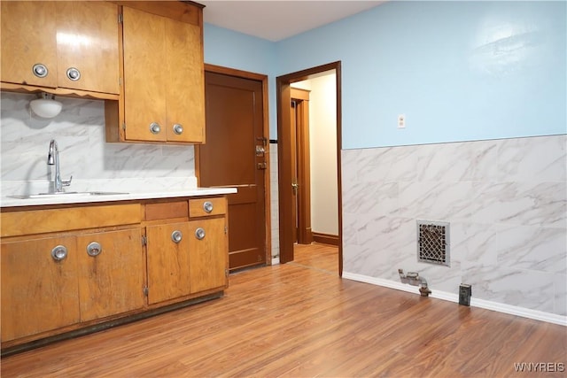 kitchen featuring light wood-type flooring, sink, and tile walls