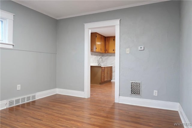 unfurnished room featuring wood-type flooring, crown molding, and sink