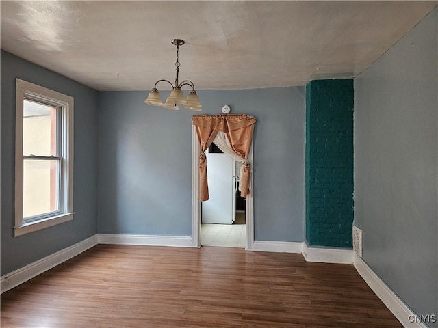 empty room featuring wood-type flooring and an inviting chandelier