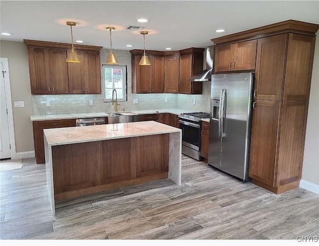 kitchen featuring pendant lighting, light hardwood / wood-style flooring, wall chimney exhaust hood, a kitchen island, and stainless steel appliances