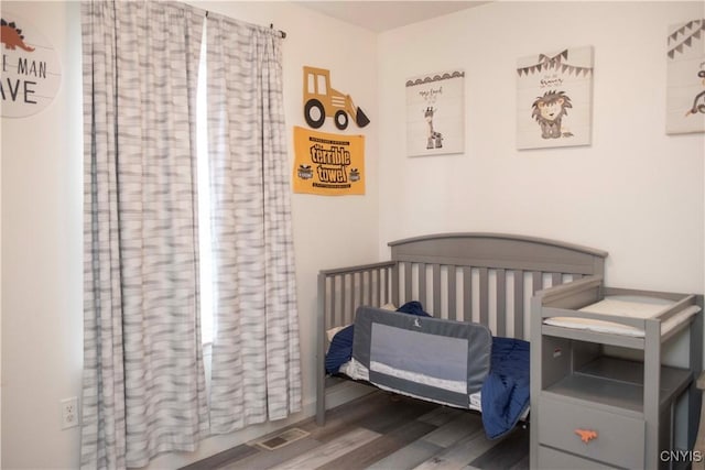 bedroom featuring a crib and dark hardwood / wood-style flooring