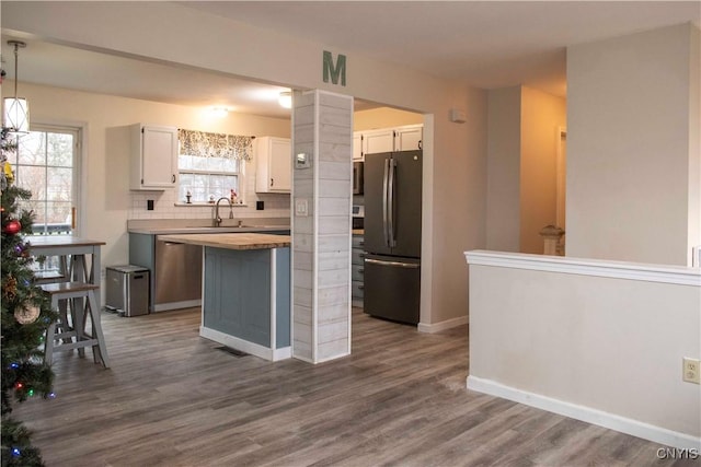 kitchen featuring white cabinetry, stainless steel appliances, tasteful backsplash, pendant lighting, and wood-type flooring