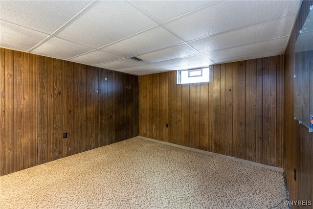 basement with a paneled ceiling, carpet floors, and wooden walls