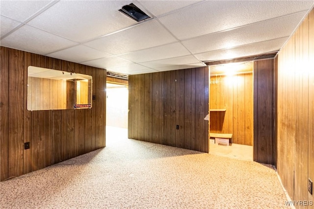 carpeted empty room with a drop ceiling and wood walls