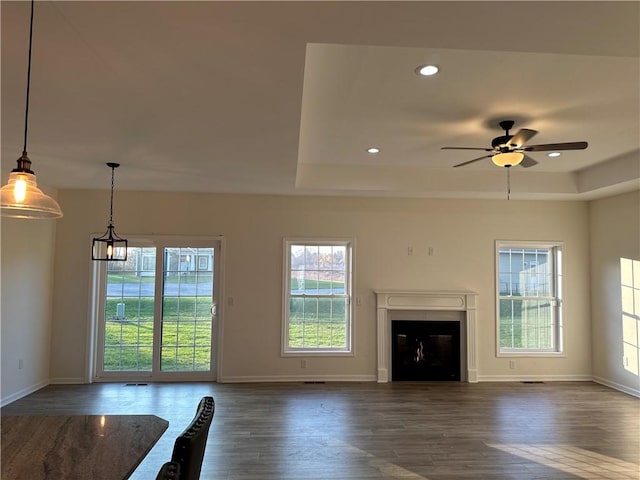 unfurnished living room featuring ceiling fan, a healthy amount of sunlight, dark wood-type flooring, and a tray ceiling