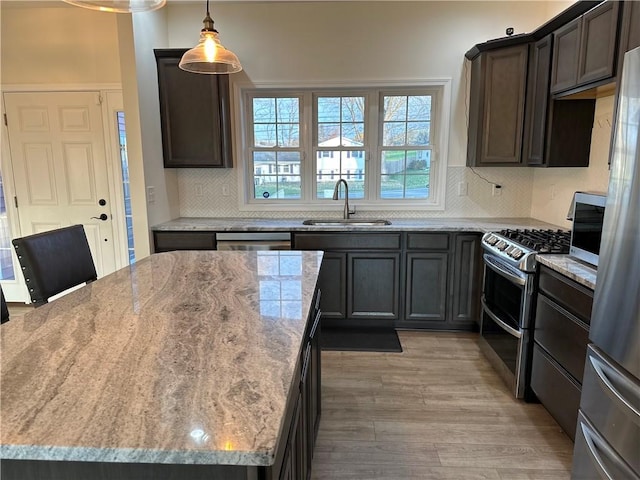 kitchen featuring hanging light fixtures, sink, decorative backsplash, light wood-type flooring, and appliances with stainless steel finishes