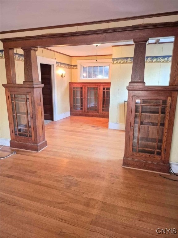 unfurnished living room with light wood-type flooring, decorative columns, and crown molding