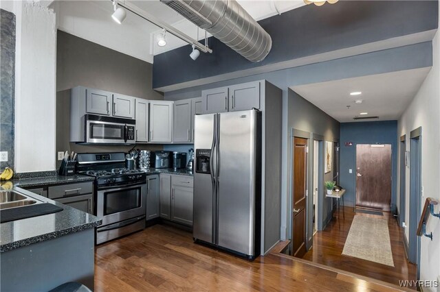 kitchen featuring gray cabinets, dark hardwood / wood-style flooring, dark stone countertops, and appliances with stainless steel finishes