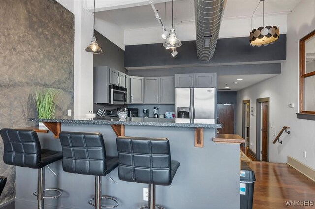 kitchen with kitchen peninsula, a kitchen breakfast bar, stainless steel appliances, gray cabinets, and hanging light fixtures