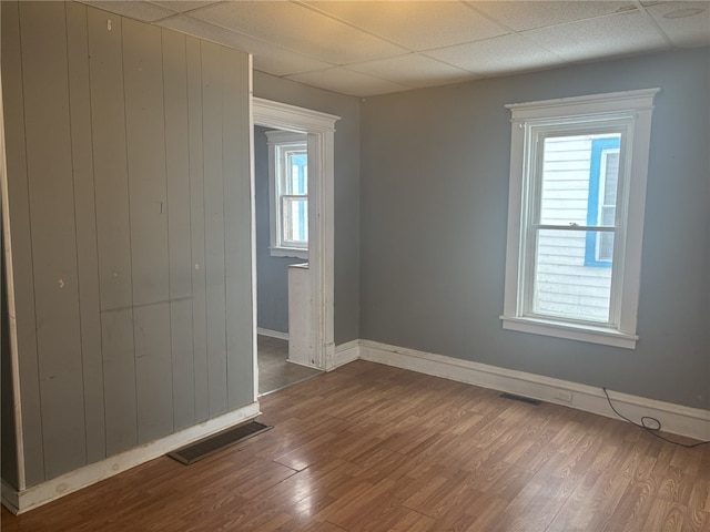 spare room featuring wood-type flooring, a wealth of natural light, and a drop ceiling