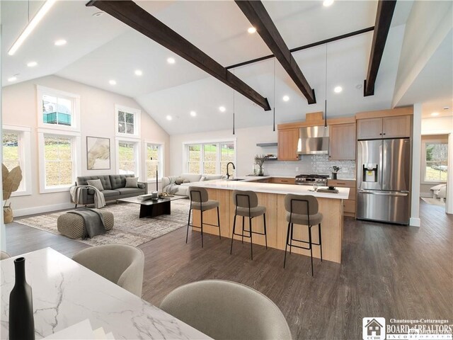 kitchen with a large island with sink, wall chimney range hood, dark hardwood / wood-style floors, appliances with stainless steel finishes, and a breakfast bar area