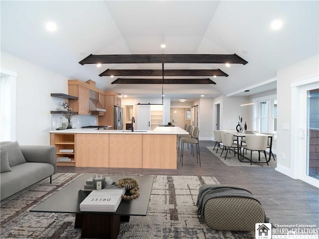 kitchen featuring appliances with stainless steel finishes, dark hardwood / wood-style floors, lofted ceiling with beams, light brown cabinetry, and wall chimney exhaust hood