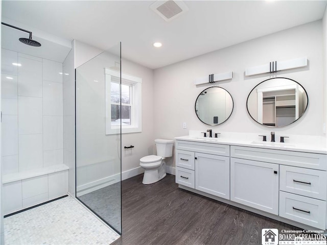 bathroom with wood-type flooring, toilet, vanity, and a tile shower