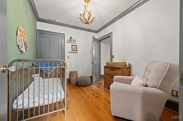 bedroom featuring hardwood / wood-style floors, an inviting chandelier, a nursery area, and ornamental molding