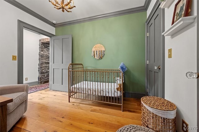 bedroom featuring ornamental molding, a nursery area, a notable chandelier, and wood-type flooring