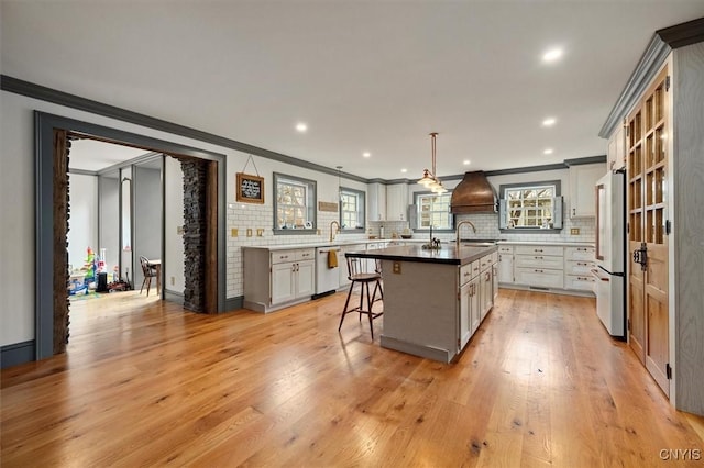 kitchen featuring stainless steel fridge, an island with sink, light hardwood / wood-style floors, and decorative light fixtures