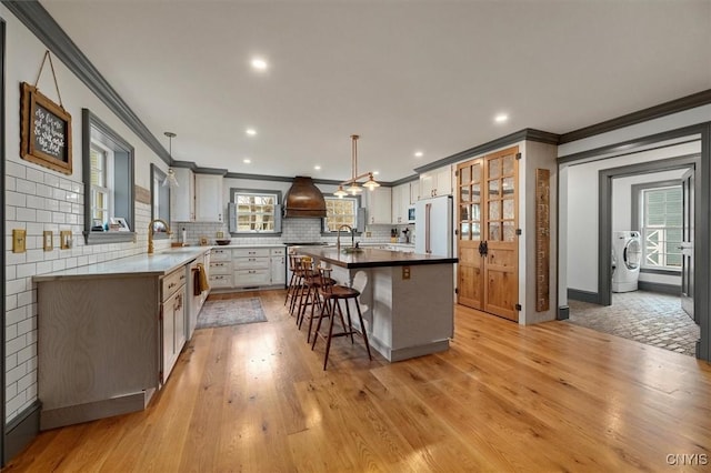 kitchen featuring a center island, white refrigerator, hanging light fixtures, light wood-type flooring, and ornamental molding