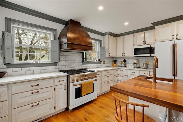 kitchen featuring premium range hood, high quality appliances, light hardwood / wood-style flooring, and crown molding