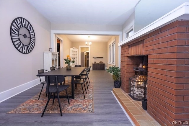 dining area with an outdoor brick fireplace, an inviting chandelier, and dark wood-type flooring