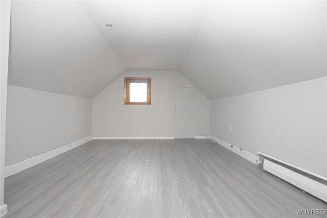 additional living space featuring baseboard heating, light hardwood / wood-style floors, and lofted ceiling