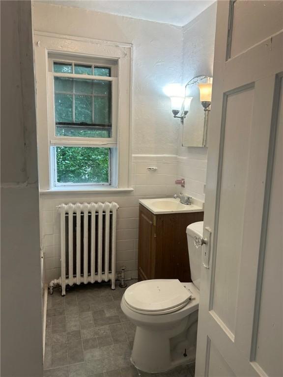 bathroom with vanity, toilet, radiator heating unit, and tile walls