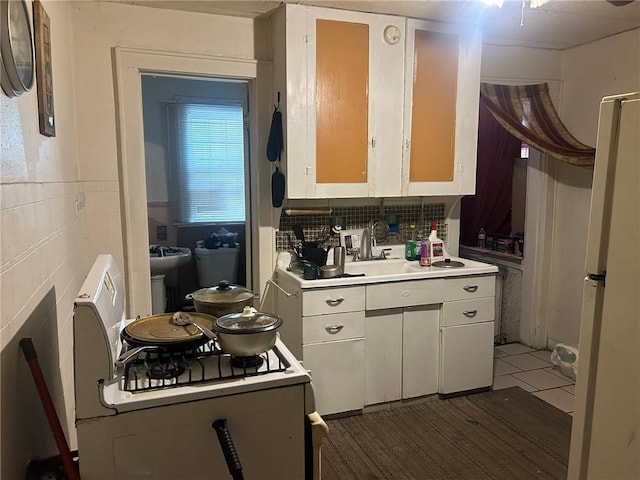 kitchen featuring sink, dark tile patterned floors, backsplash, white cabinets, and range