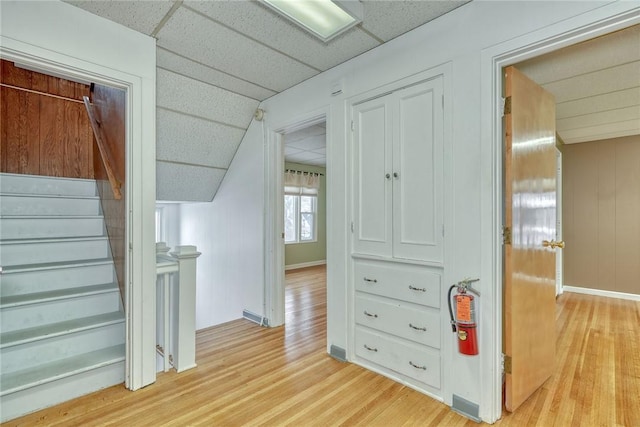 corridor with a paneled ceiling, light hardwood / wood-style floors, and wooden walls