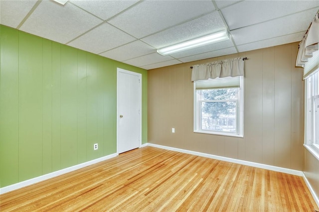 spare room with a healthy amount of sunlight, a drop ceiling, and light hardwood / wood-style floors