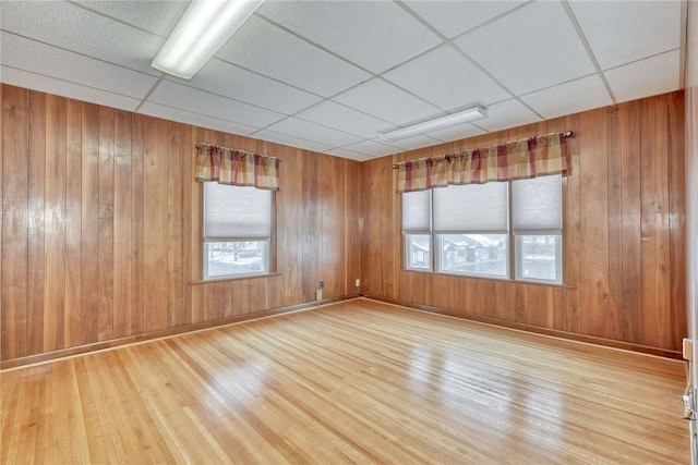 empty room featuring wood walls, a drop ceiling, and light wood-type flooring